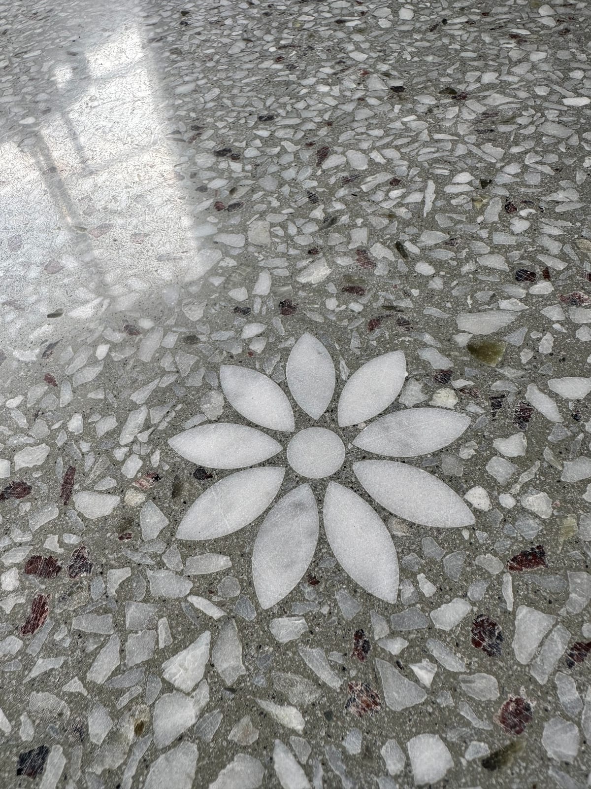 Nærbilde av blomstermotiv i hvit marmor lagt inn i polert grå terrazzo med store steinflak