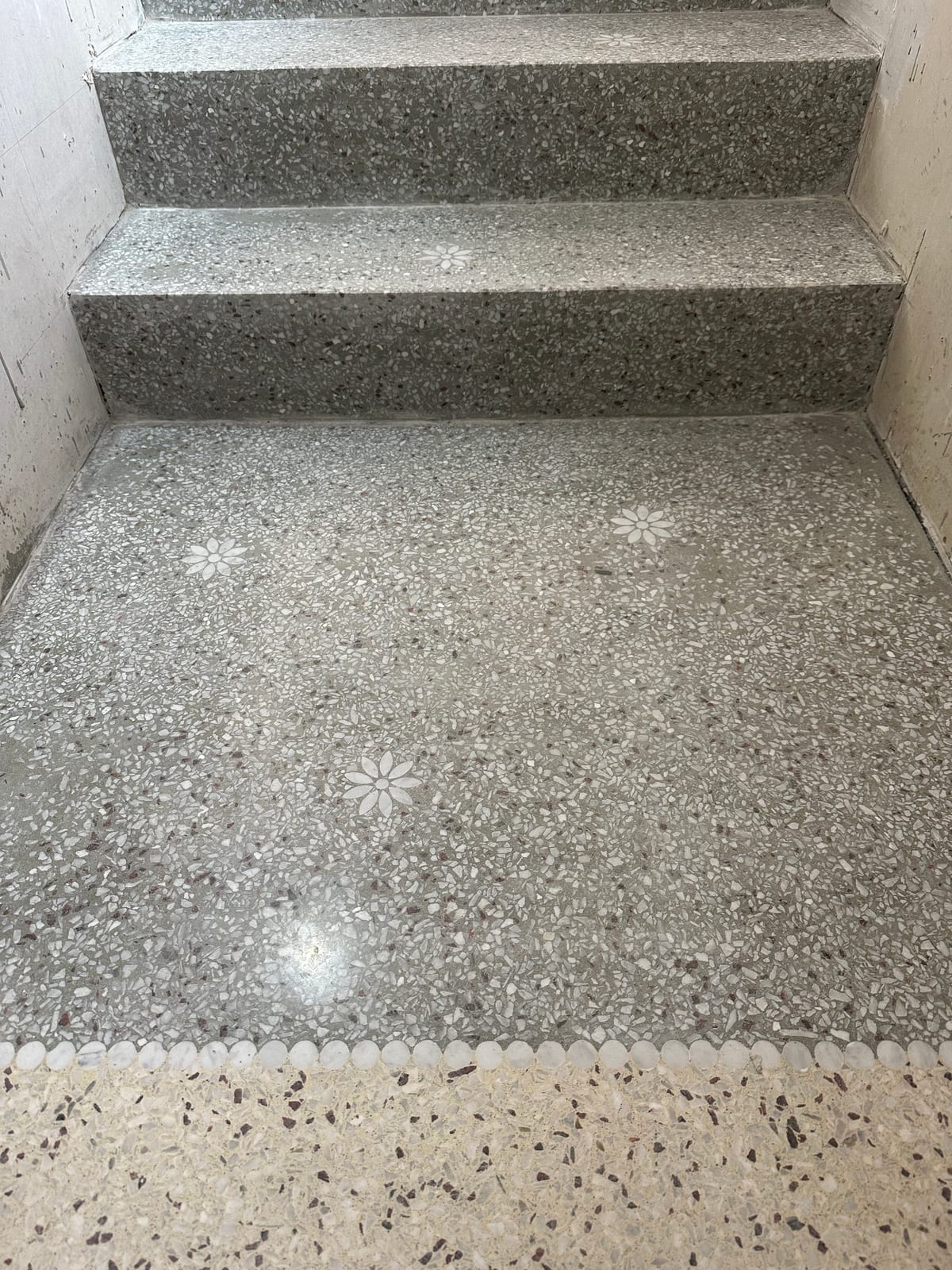 Grå terrazzotrapp og repos med innlagte hvite blomstermotiver, avgrenset mot lys terrazzo med en rad hvite steinperler